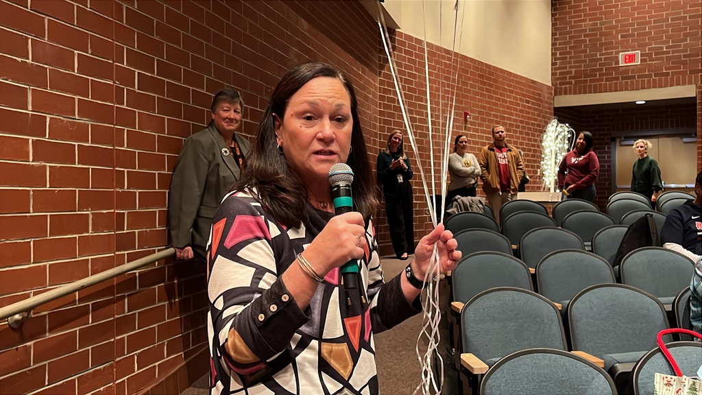 A woman speaks in an auditorium where many more people are standing and clapping.