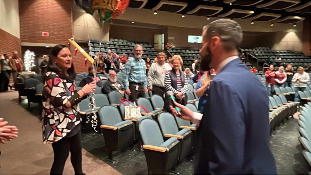 A man walks up to congratulate a woman in an auditorium where many more people are standing and clapping.