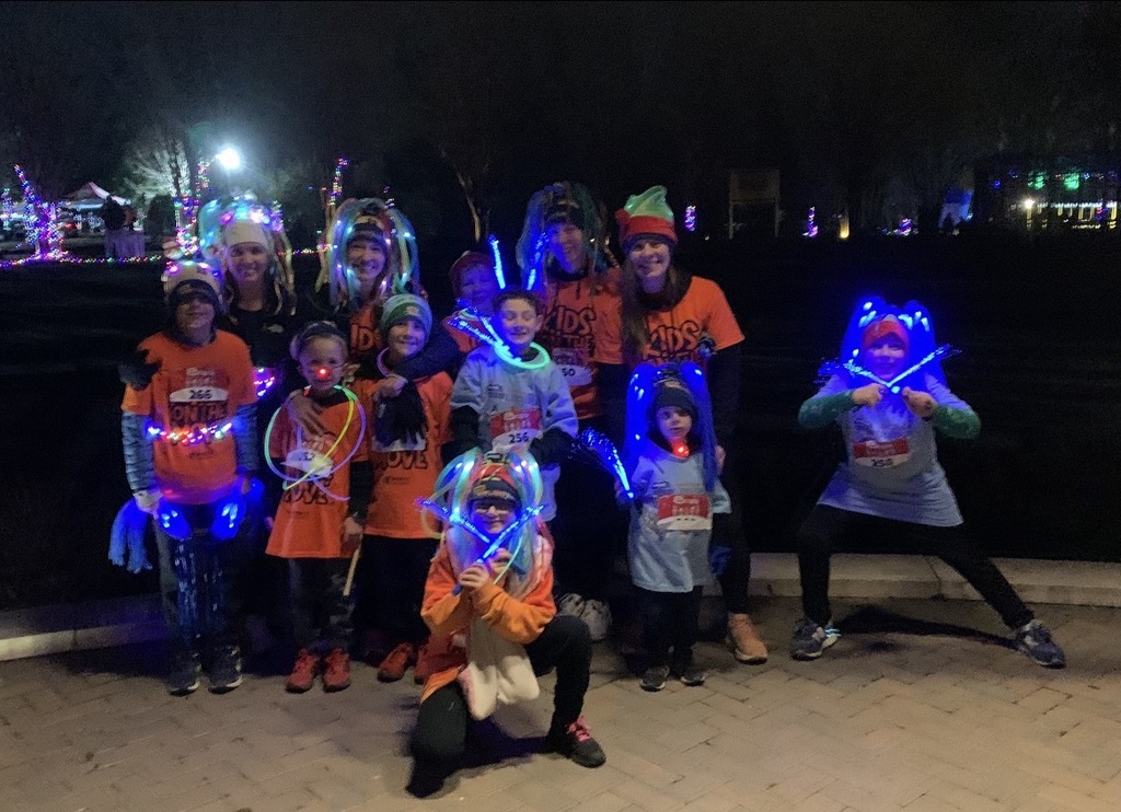A group of students and one teacher wearing Kids on the Move shirts pose for a photo at night.