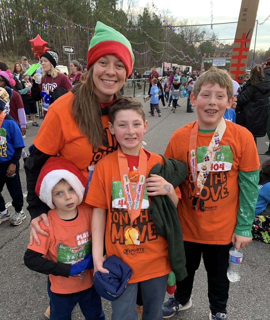 Students  and an adult wearing Kids on the Move shirts pose for a photo after a race.