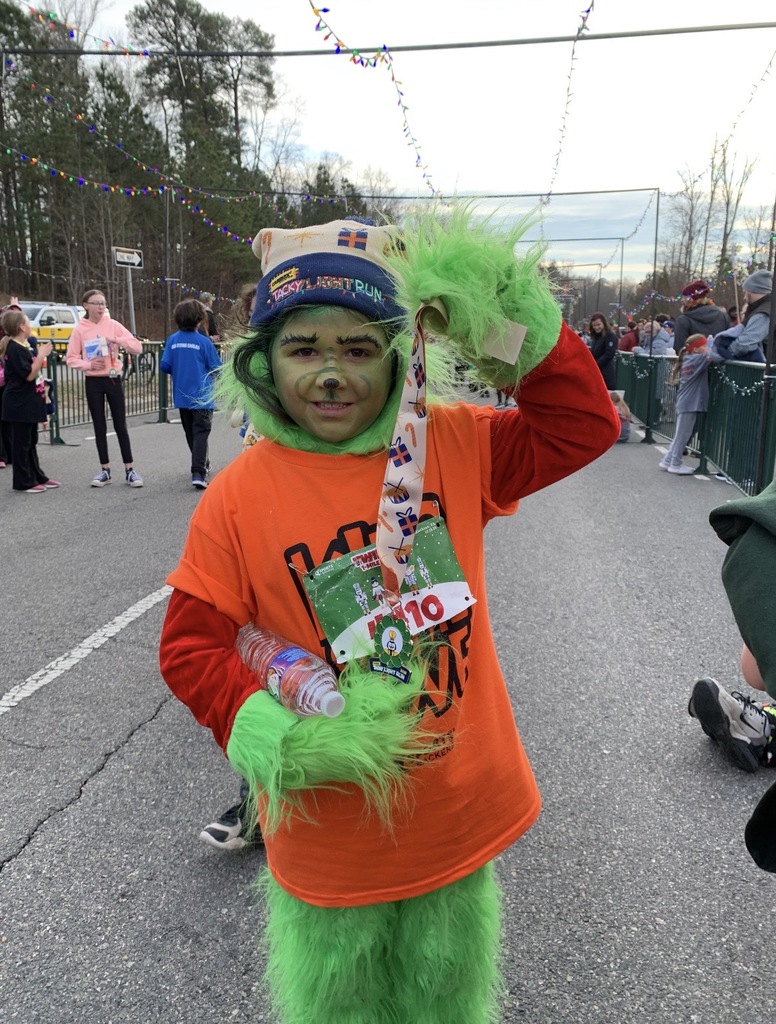 A student  wearing a Kids on the Move shirt and Grinch makeup poses for a photo after a race.