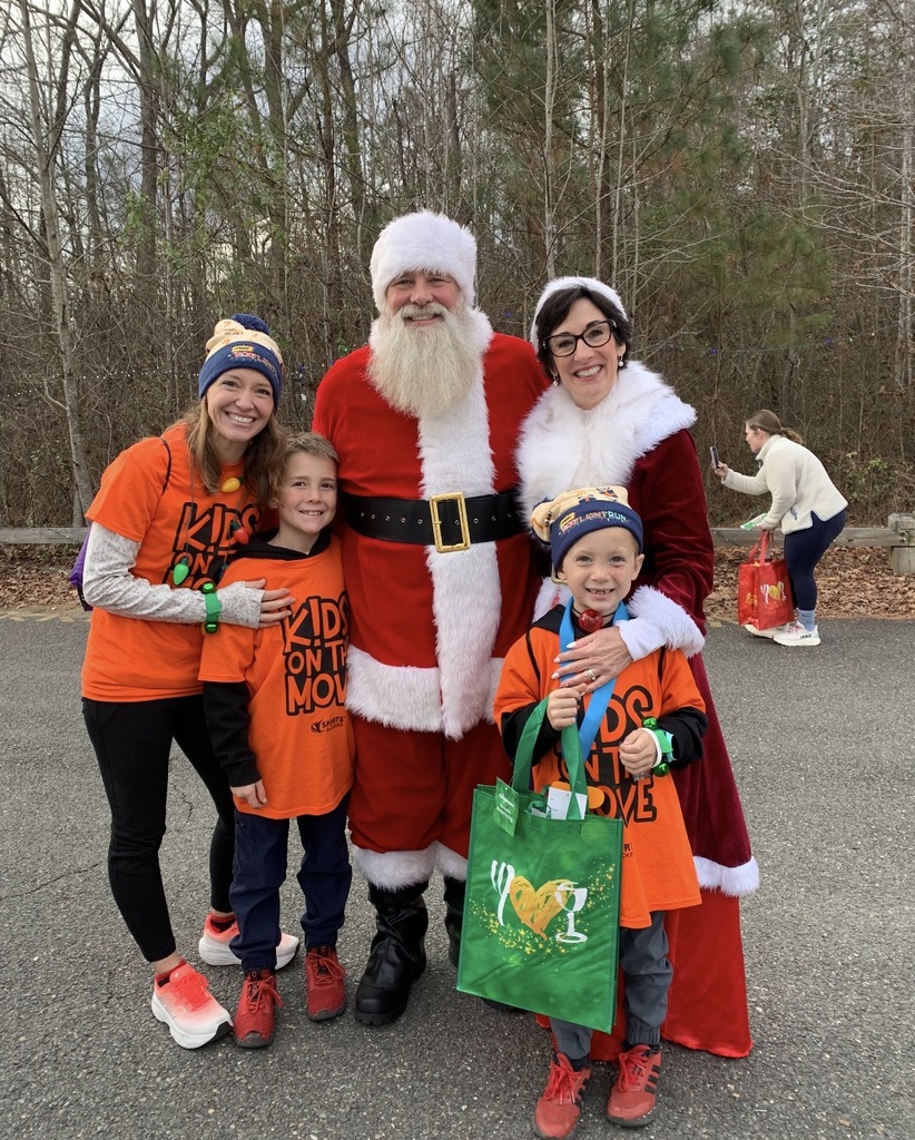 Two students and one teacher wearing Kids on the Move shirts pose for a photo with Santa and Mrs. Claus. 