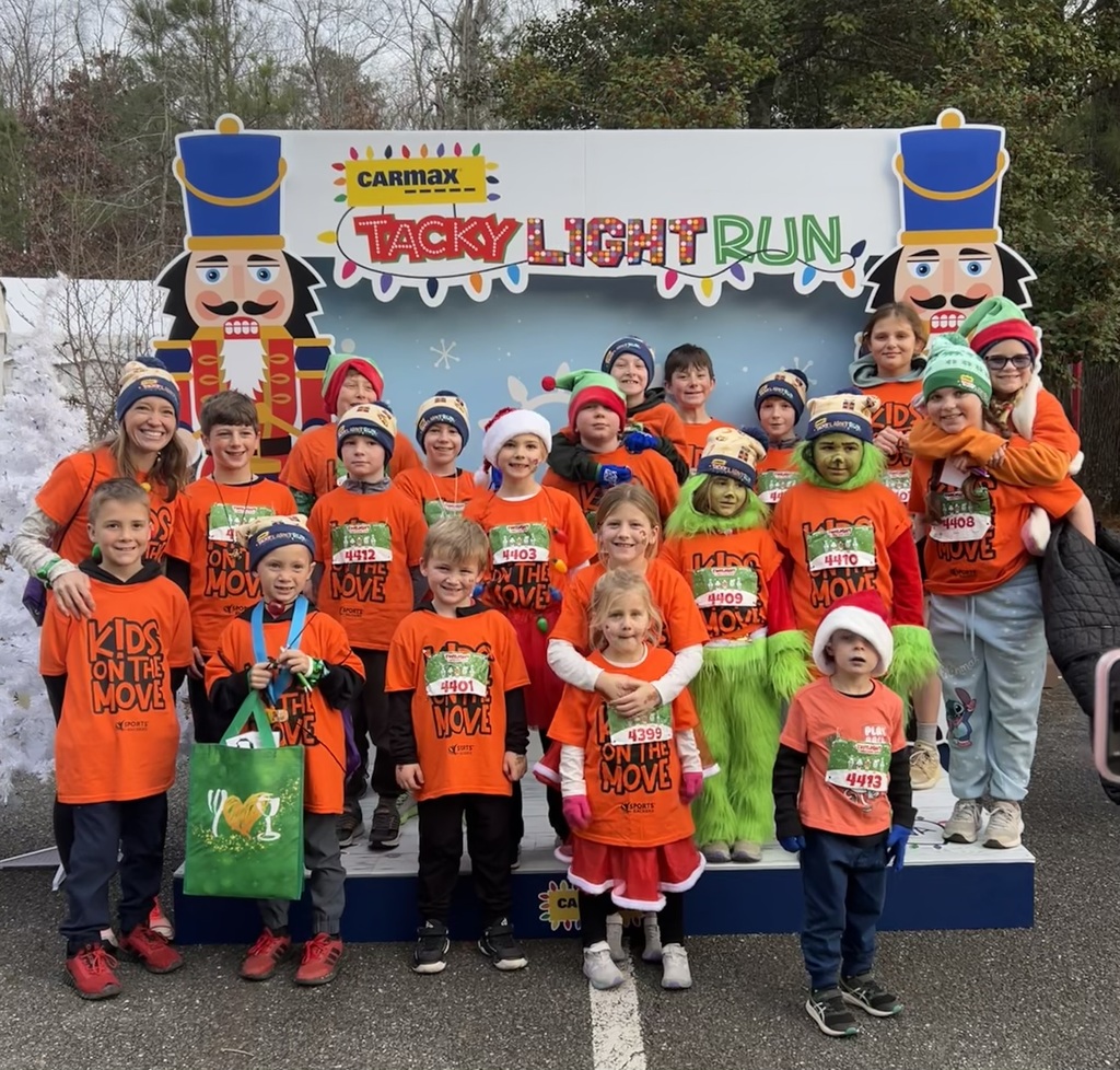 A group of students and one teacher wearing Kids on the Move shirts pose for a photo.