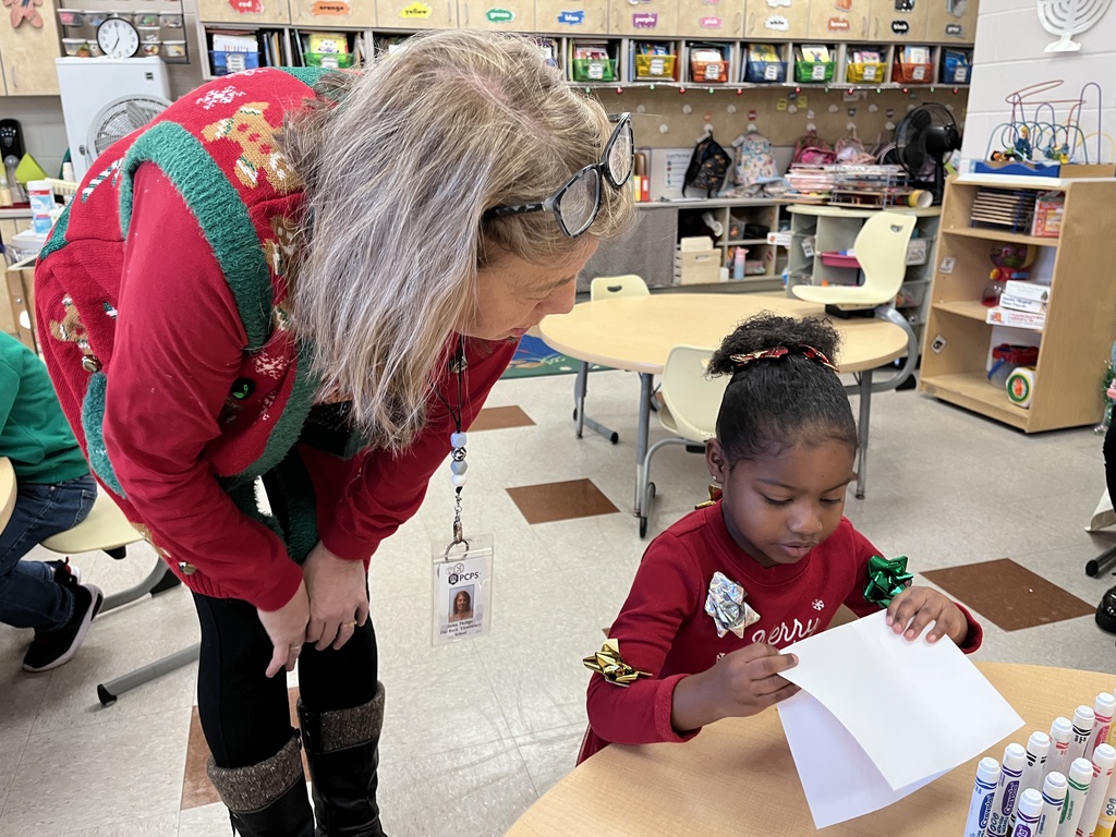 A preschooler makes a card for their student teacher. An adult helps. 