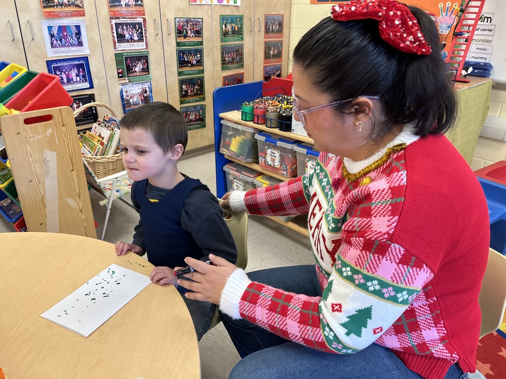 A preschooler makes a card for their student teacher. An adult helps. 