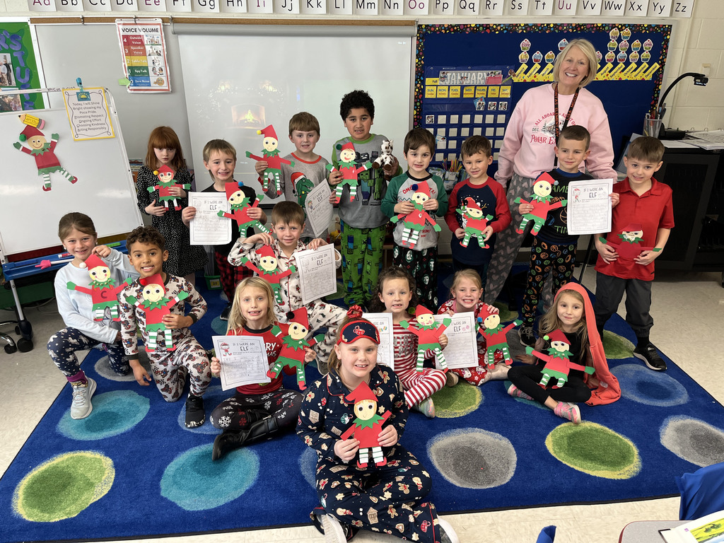 A class poses for a group photo while holding up elves and a writing assignment they made in class. 
