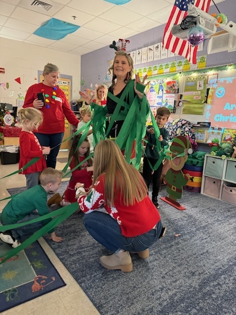 Adults and children de corate a teacher as a Christmas tree.