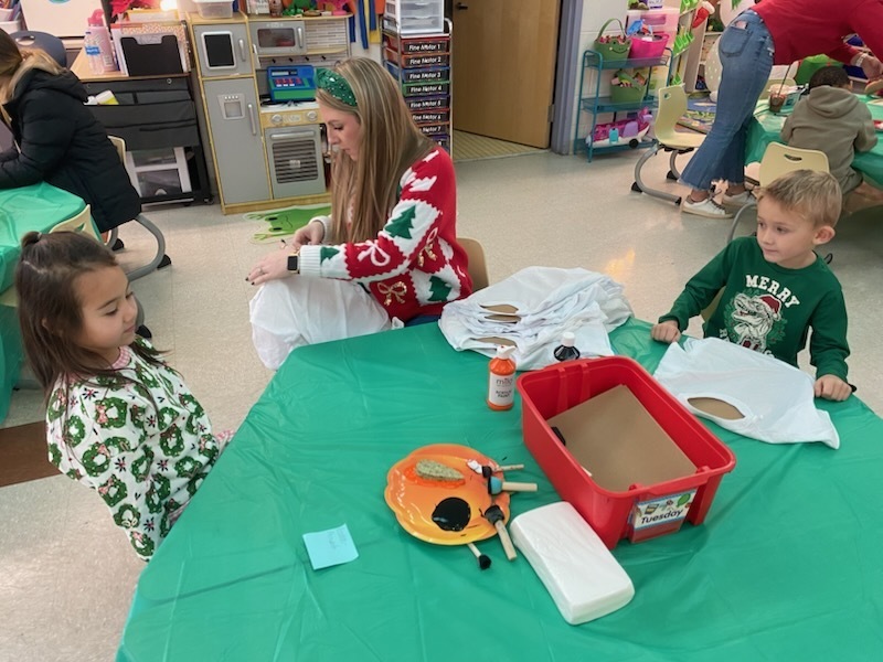 An adult helps students work on craft projects.