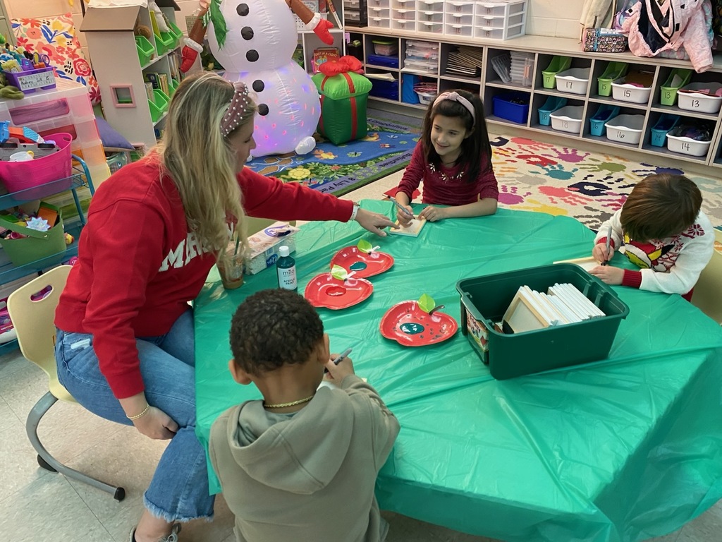 An adult helps students work on craft projects.