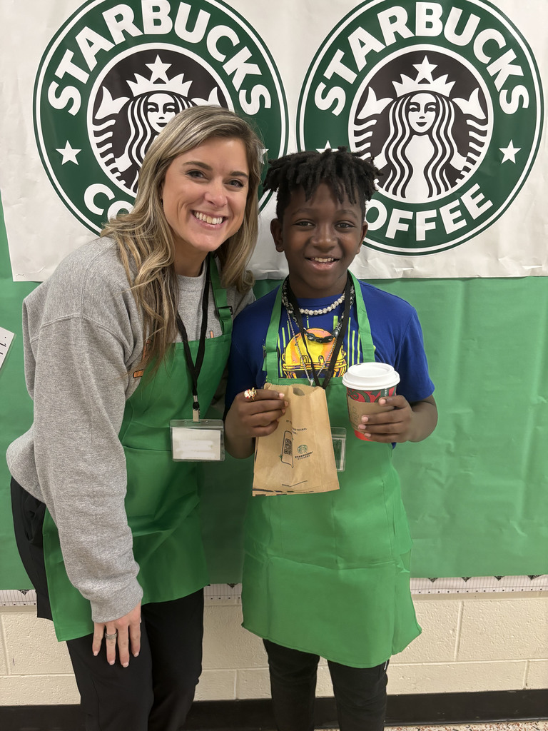 A student and teacher pose for a photo in front of a Starbucks themed bulletin board.