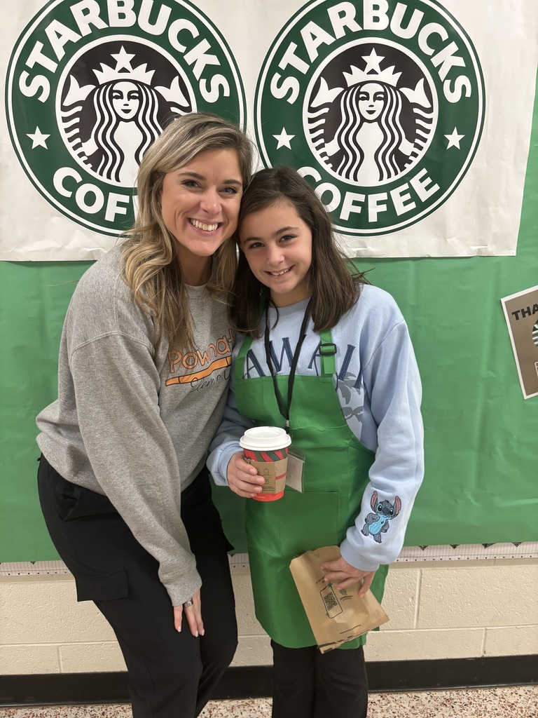 A student and teacher pose for a photo in front of a Starbucks themed bulletin board.