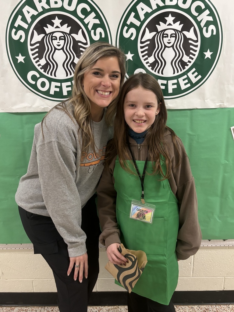 A student and teacher pose for a photo in front of a Starbucks themed bulletin board.