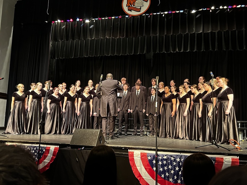 A choir director leads a group of choir students in a performance.