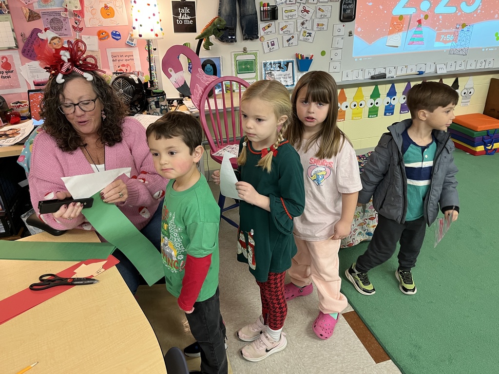 A teacher helps students make their elf hats. 