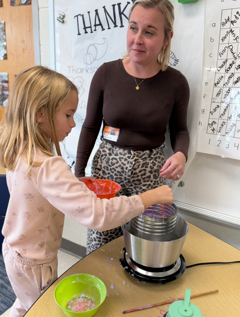 A first grader participates in a colonial craft day activity.  An adult helps.