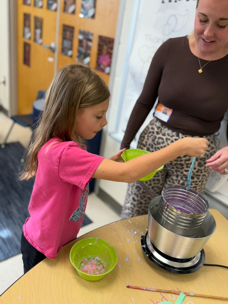 A first grader participates in a colonial craft day activity.  An adult helps.