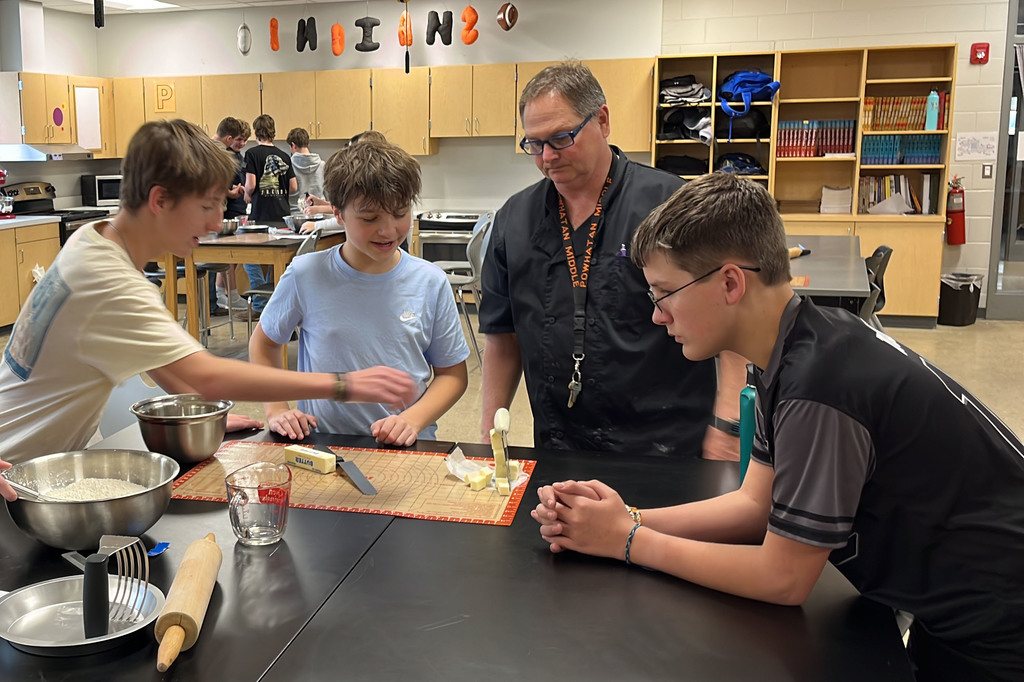 Students in a family and consumer sciences class work together to make pie dough from scratch. A teacher helps.