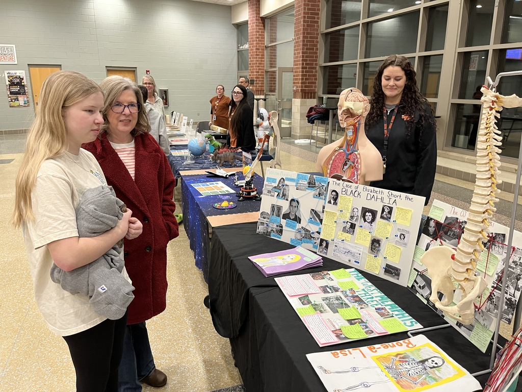 An employee talks to a student and adult at a booth at a high school information night.