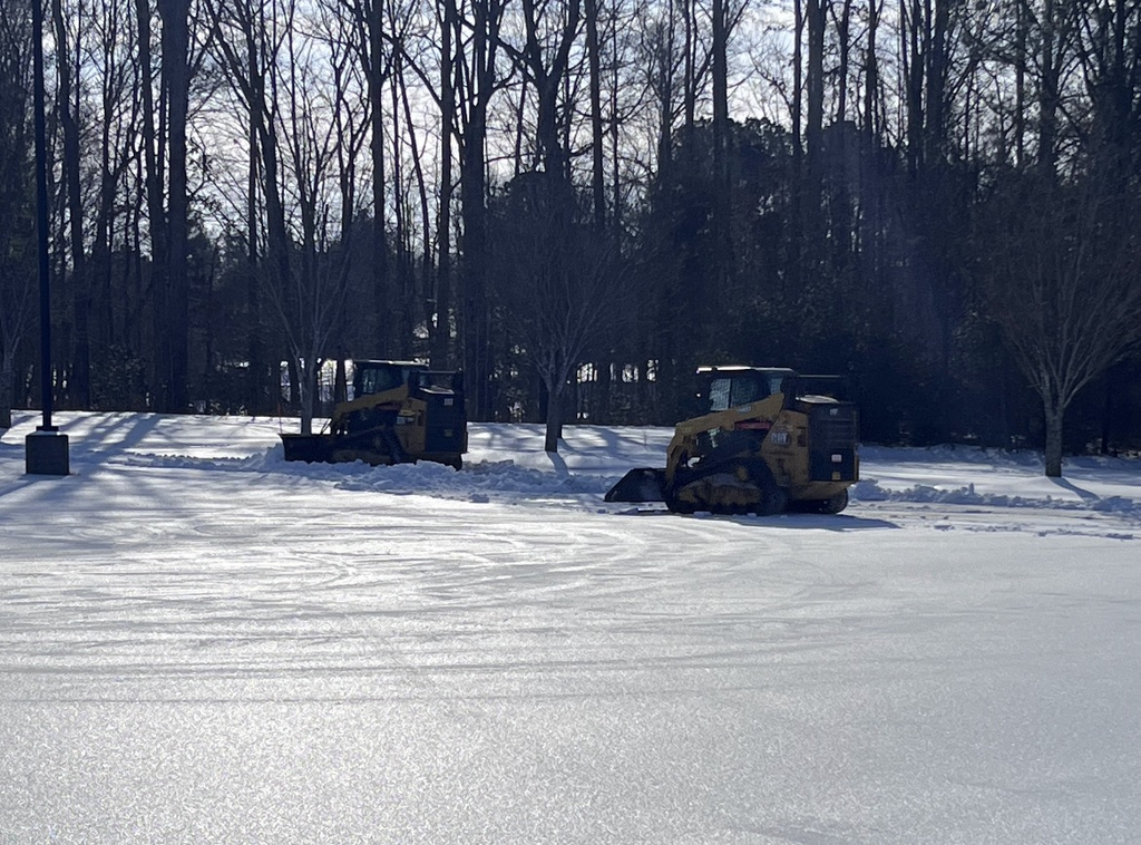 Photo of a school parking lot covered in ice and snow being cleared. 