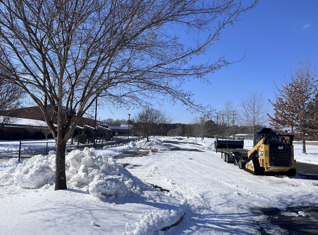 Photo of a school parking lot covered in ice and snow being cleared. 