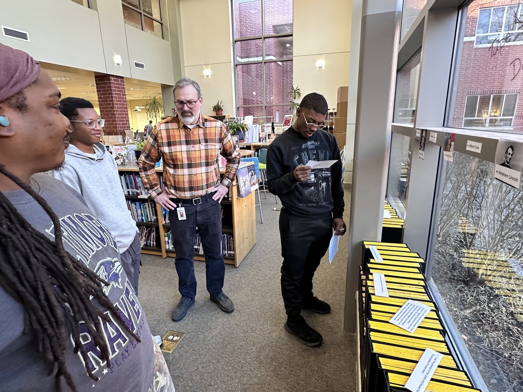 Students participate in a Civil War scavenger hunt in the school library. Two adults help.