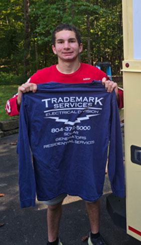 A student poses for a photo holding a shirt with a company logo representing where he is doing a Youth Registered Apprenticeship.