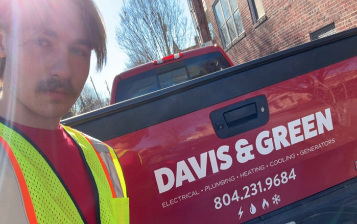 A student poses for a photo in front of a company logo representing where he is doing a Youth Registered Apprenticeship.