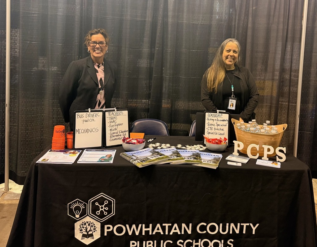 Two women stand behind a PCPS table ts at a job fair.
