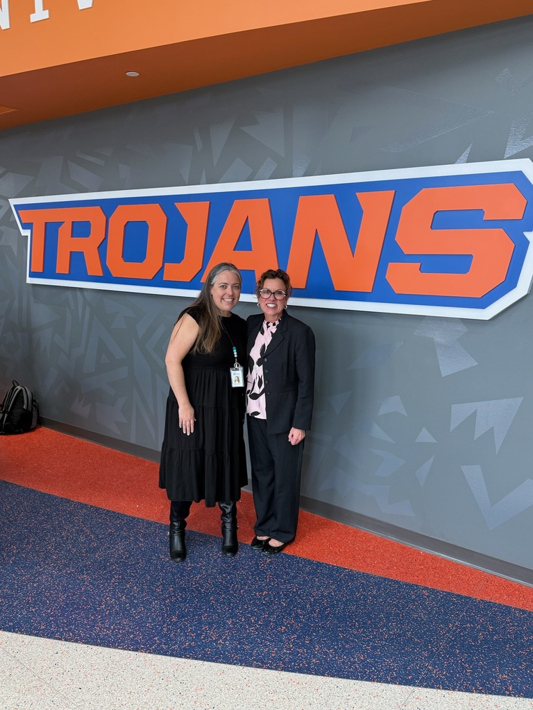 Two women pose for a photo underneath a Trojans sign.