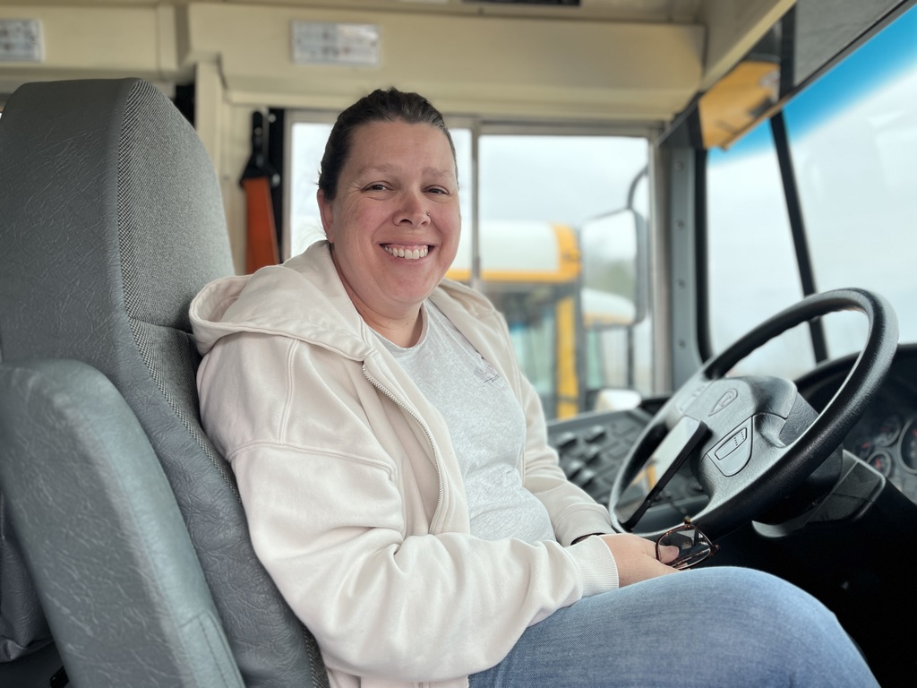 A school bus driver poses for a photo on a school bus.