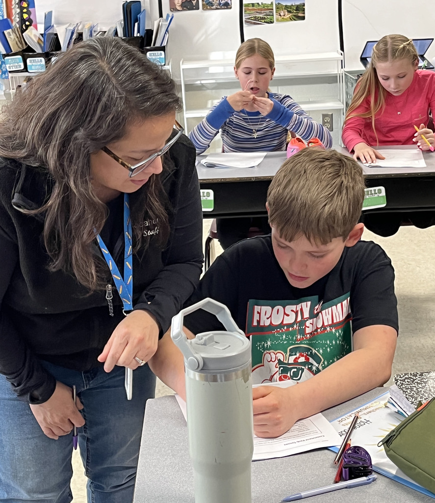 Students work on a lesson focused on strengthening grammar skills by working on consistent verb tenses. A teacher helps a student.