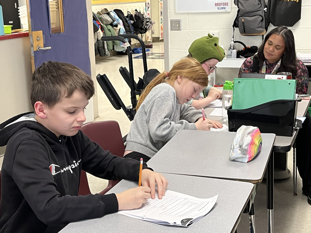 Students work on a lesson focused on strengthening grammar skills by working on consistent verb tenses. A teacher helps a student.
