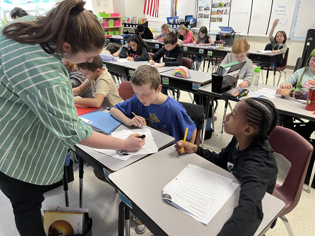 Students work on a lesson focused on strengthening grammar skills by working on consistent verb tenses. A teacher helps a student.