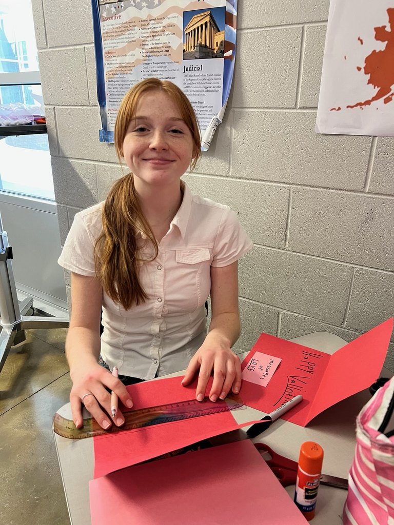 A student poses for a photo holding a valentine made for a veteran.