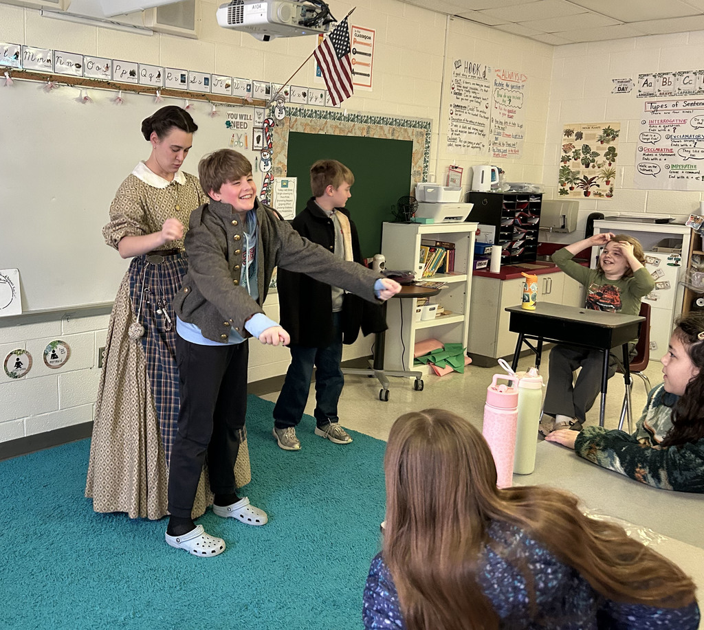A historian helps a student try on a coat while  introducing a class to the subject of the Civil War. 