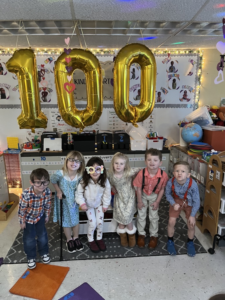 Children dressed up for the 100th day of school pose for a photo under balloons spelling 100.