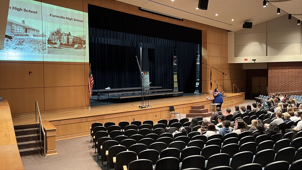 A guest presenter speaks to students in a crowded auditorium.