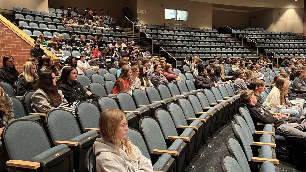 Students in a crowded auditorium listen to a guest presenter.