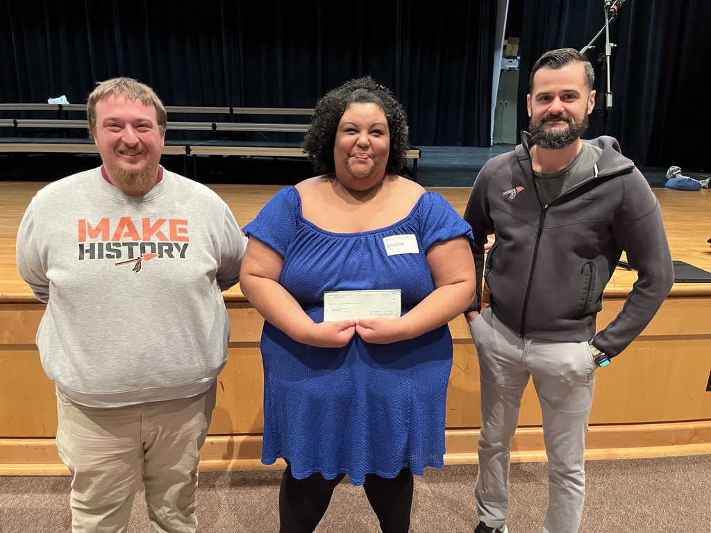 A guest presenter poses with two adults while holding a check.