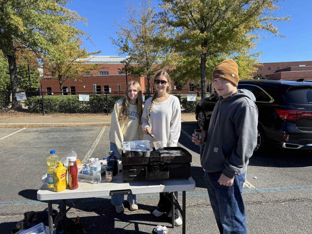 Students in a parking lot prepare food for an outdoor cookout fundraiser.
