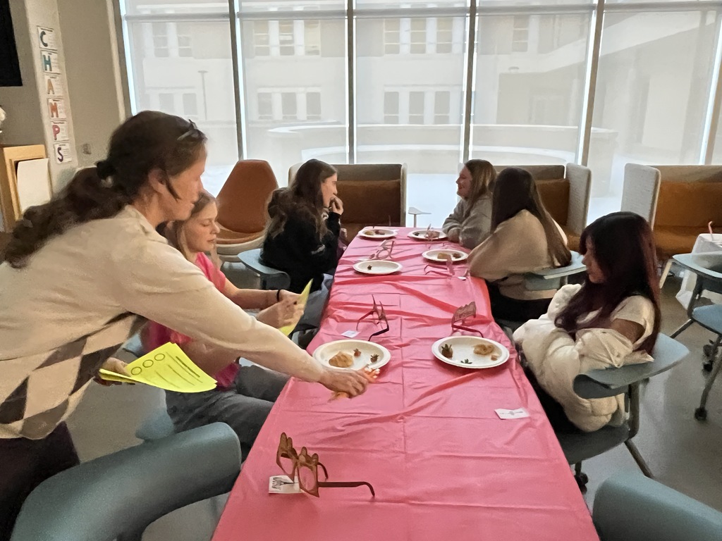 Students in French calss meet in the library to help choose a semester book. An adult serves them criossants.