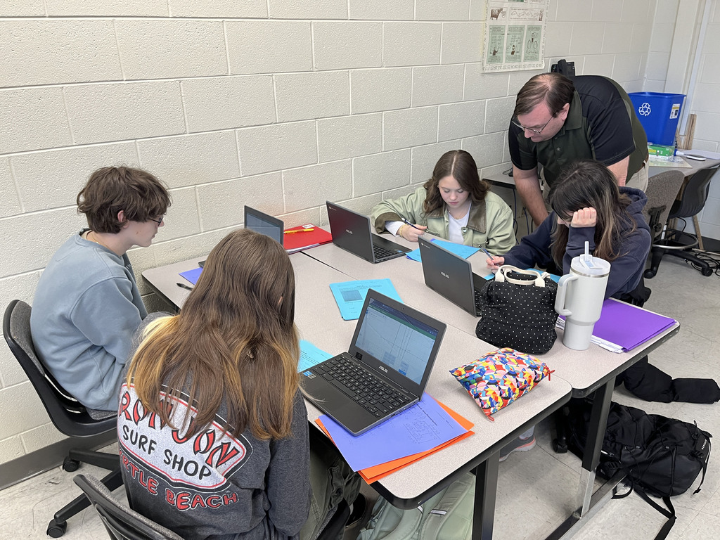 Algebra II classes work in groups to review polynomial operations and division through rotating stations A teacher helps..
