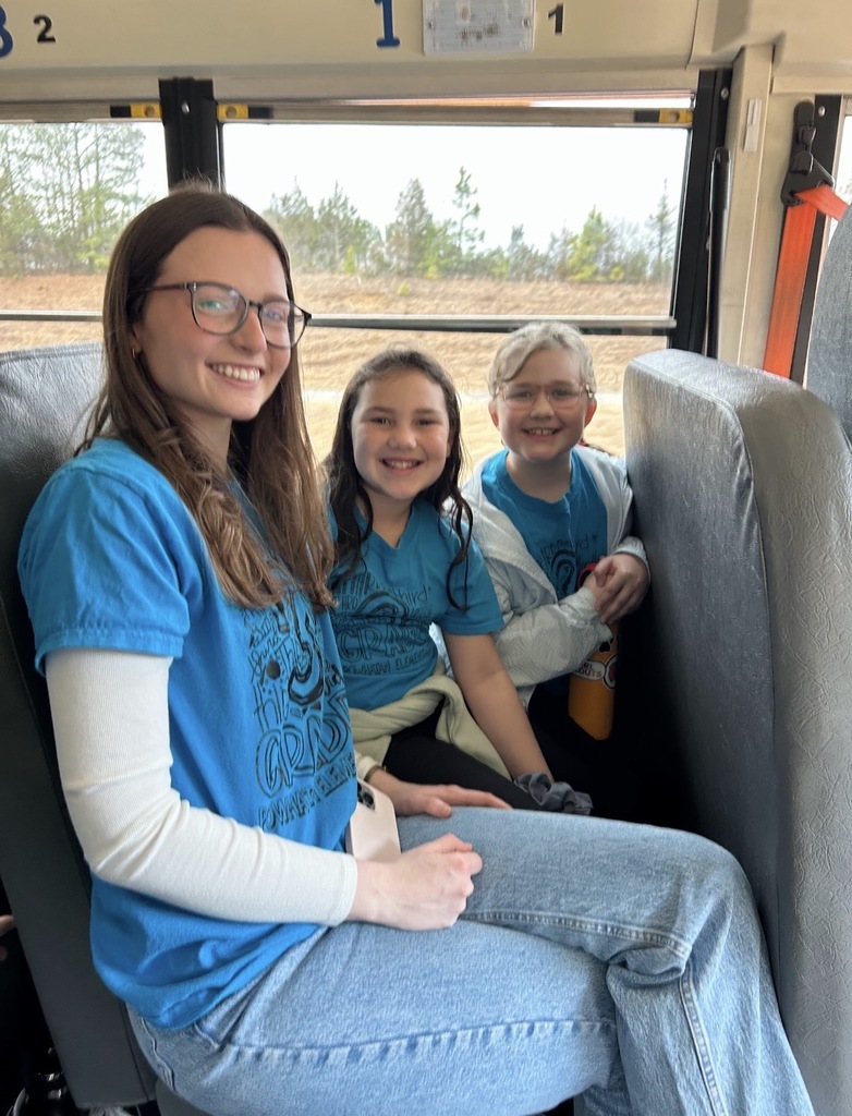 A teacher and two students pose for a photo on a school bus. 