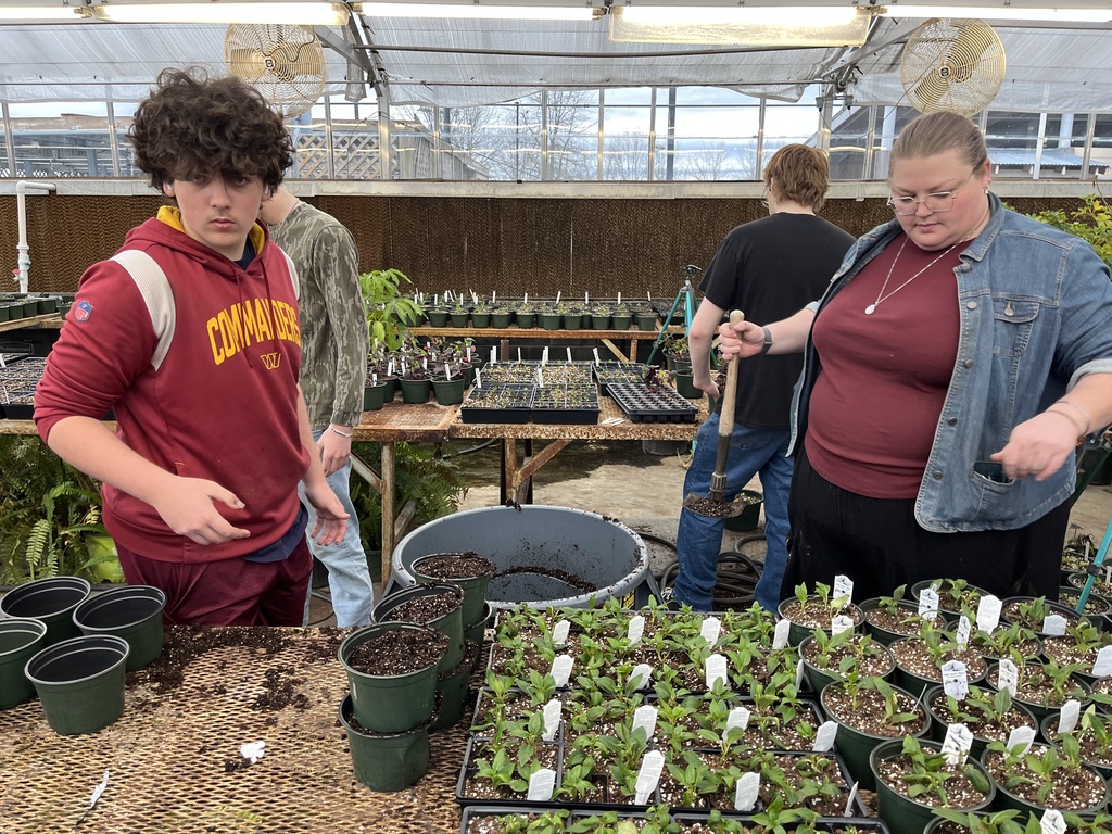 Students and a teacher work with plants being grown to sell in a plant sale.