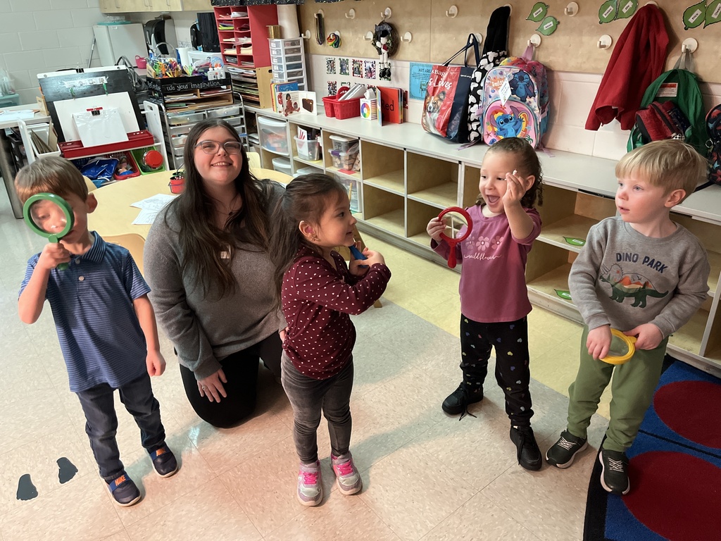 Preschoolers pose for a photo with large magnifying glasses. A high school student is also with them.
