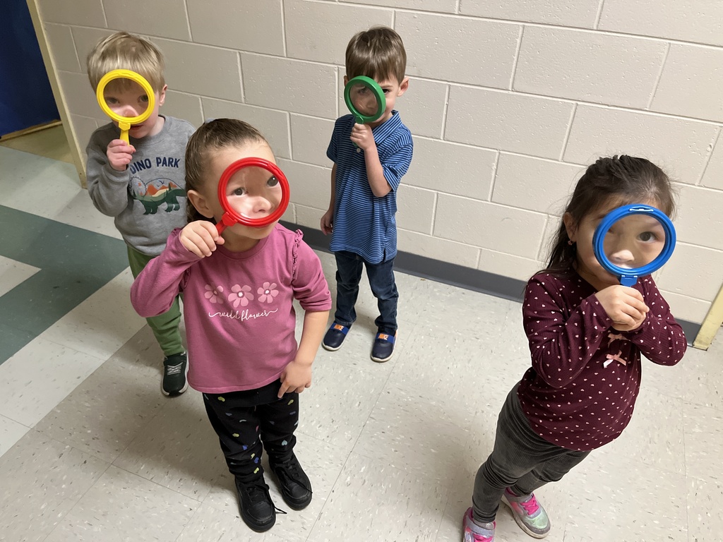 Preschoolers pose for a photo with large magnifying glasses.
