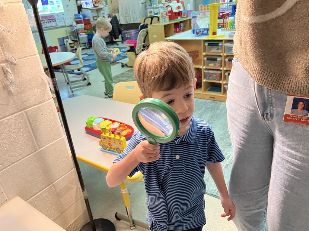 A preschooler  uses a large magnifying glass to help find a missing class toy.