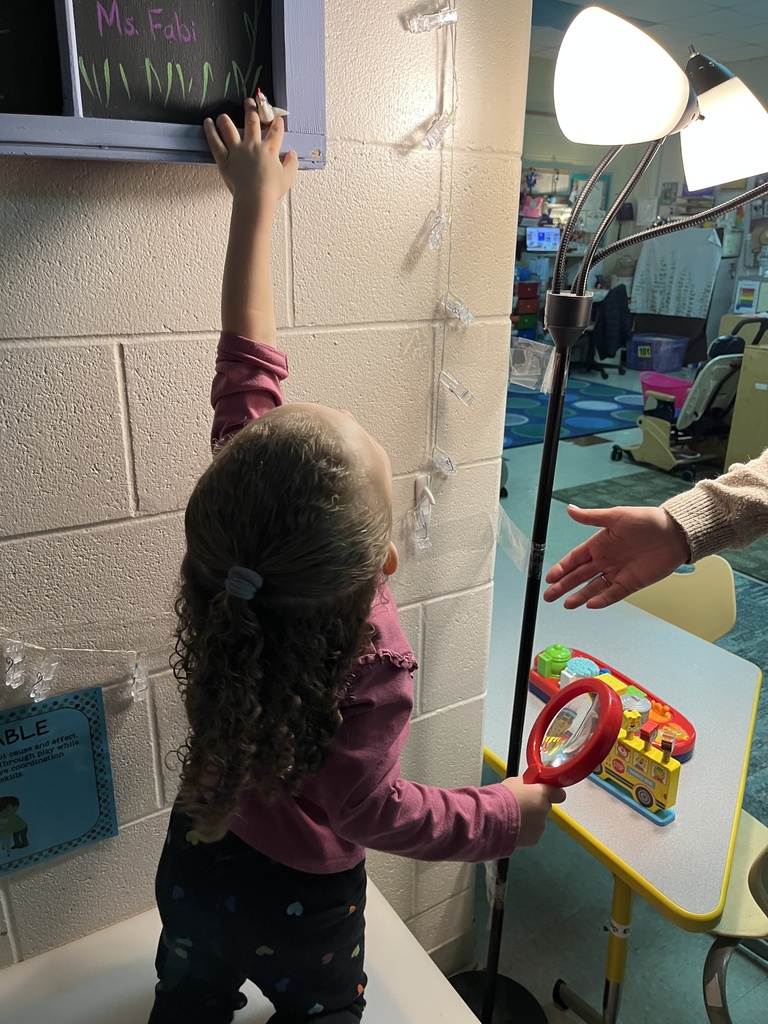 A preschooler  uses a large magnifying glass to help find a missing class toy.