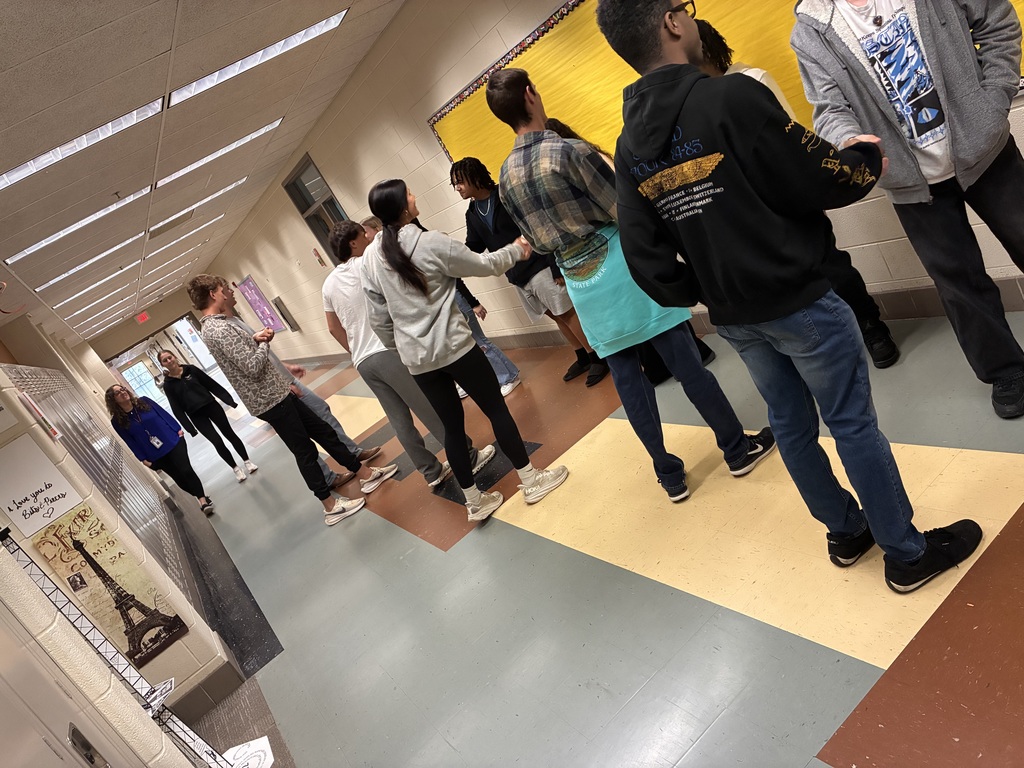 Students work in pairs to practice handshake skills in a school hallway.