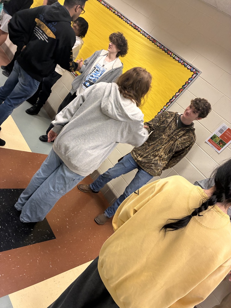 Students work in pairs to practice handshake skills in a school hallway.